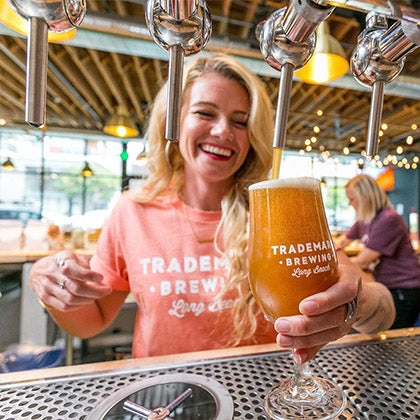 Photo of fabulous Trademark Brewing beertender pouring a frothy beer off of the tap