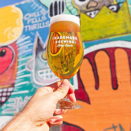 Photo of hand holding beautiful pint of Trademark beer in front of colorful outdoor mural