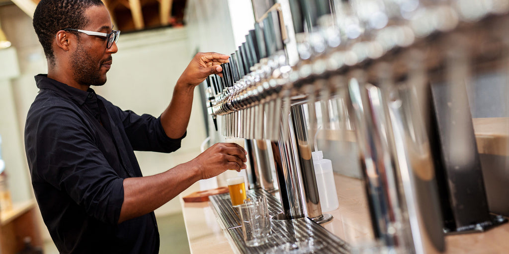 Image of very handsome man pouring a beer off of one tap in a long line of taps behind the bar