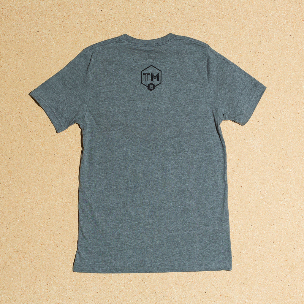 Photo of heather gray t-shirt with large Trademark Brewing shield logo on back side
